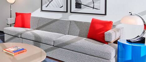 A modern living room with a grey sofa, red cushions, a round coffee table, and two framed abstract artworks on the wall.