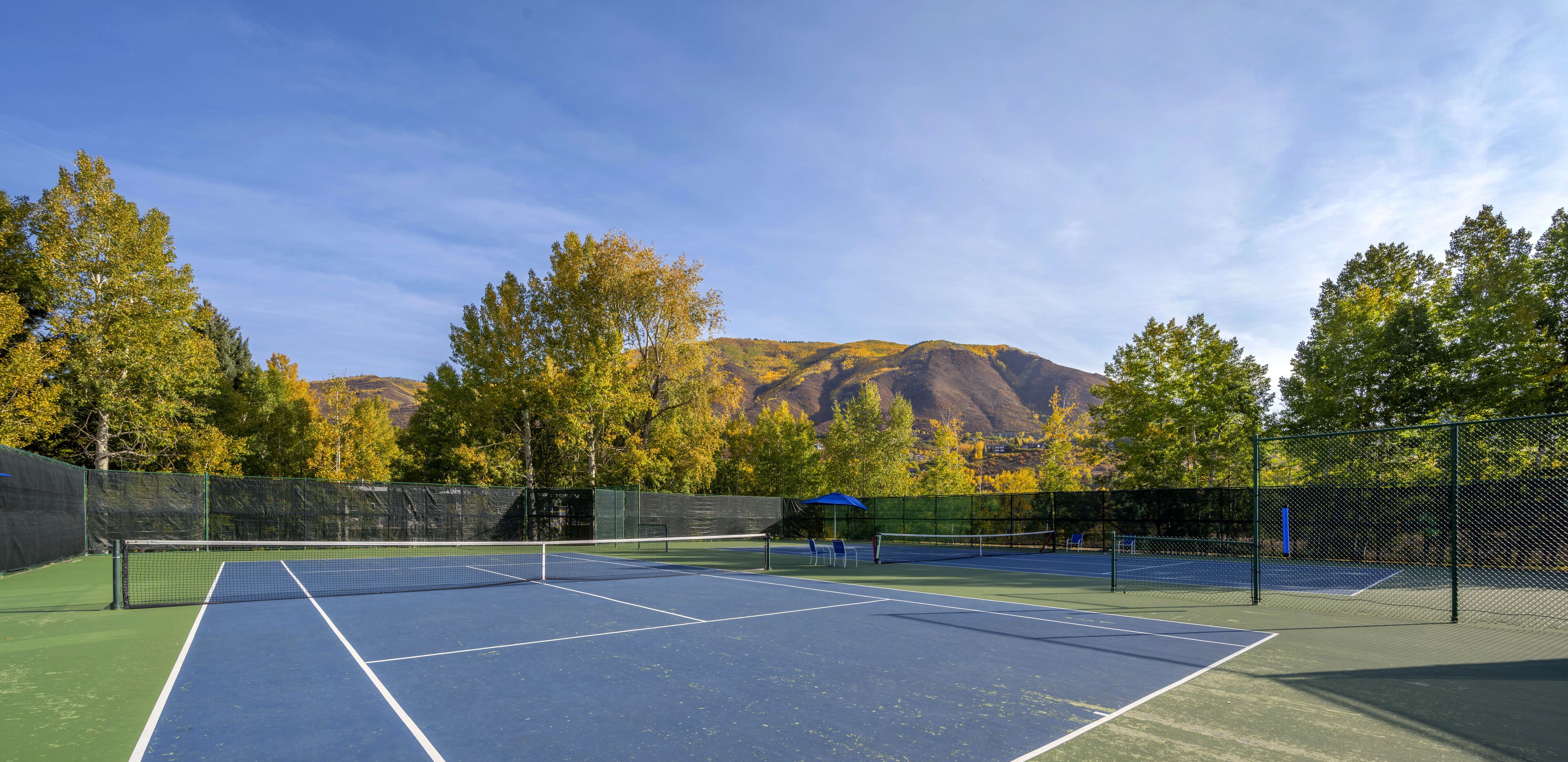 Un court de tennis en plein air, doté d’un filet, entouré d’arbres et avec une montagne en arrière-plan.