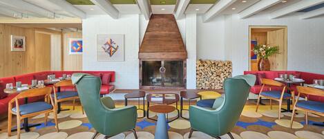 Un interior moderno con asientos rojos, sillas verdes y una chimenea central.