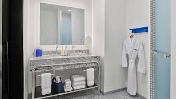 A modern bathroom with a marble countertop, a large mirror, a towel rack, and a robe hanging on the wall.
