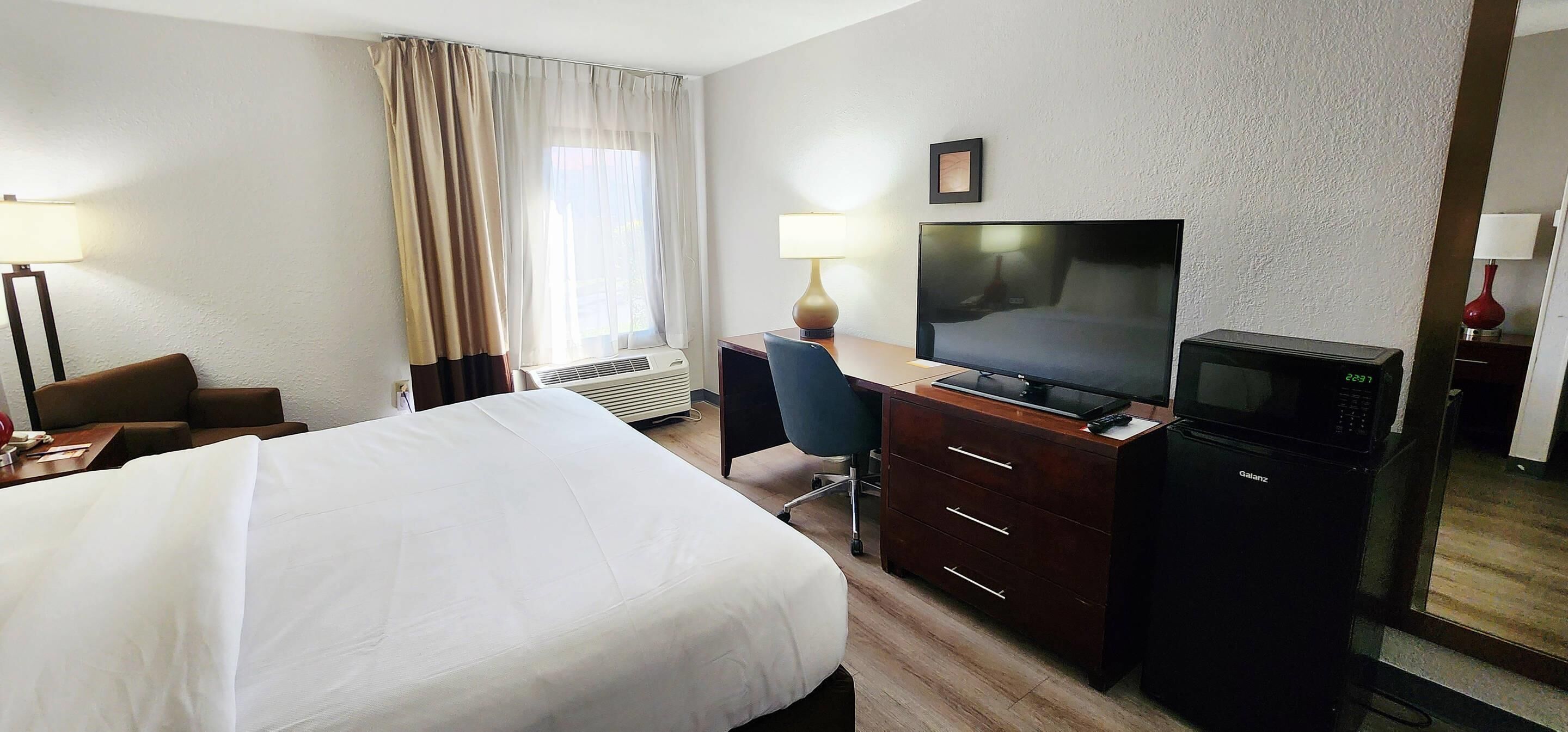 Habitación de hotel con cama, escritorio, televisor, microondas y una ventana grande con cortinas.
