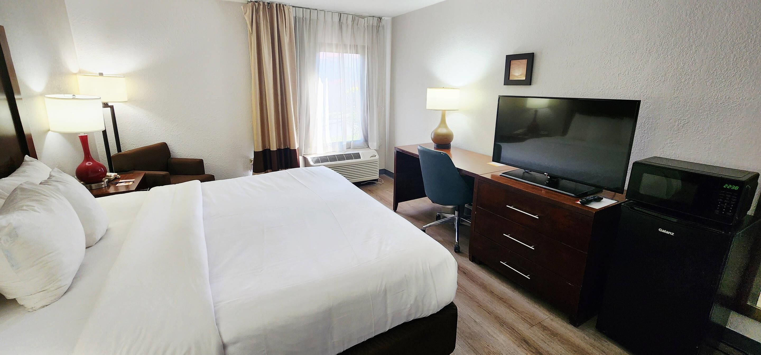 Ett hotellrum med en säng, ett skrivbord med en tv, en stol, en skrivbordslampa och en mikrovågsugn.