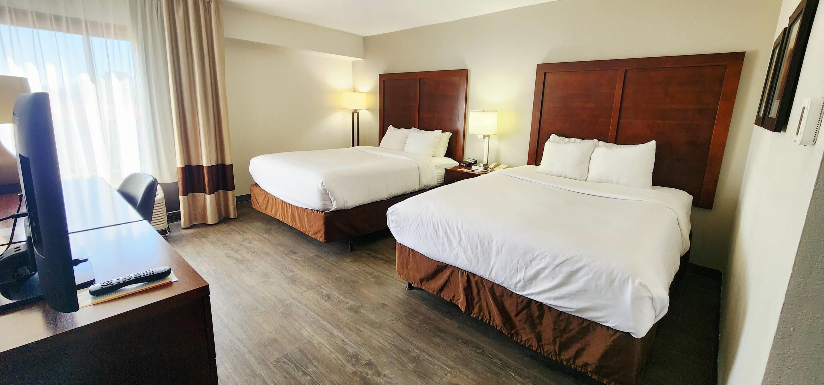 A hotel room with two beds, a desk with a TV, and a lamp.