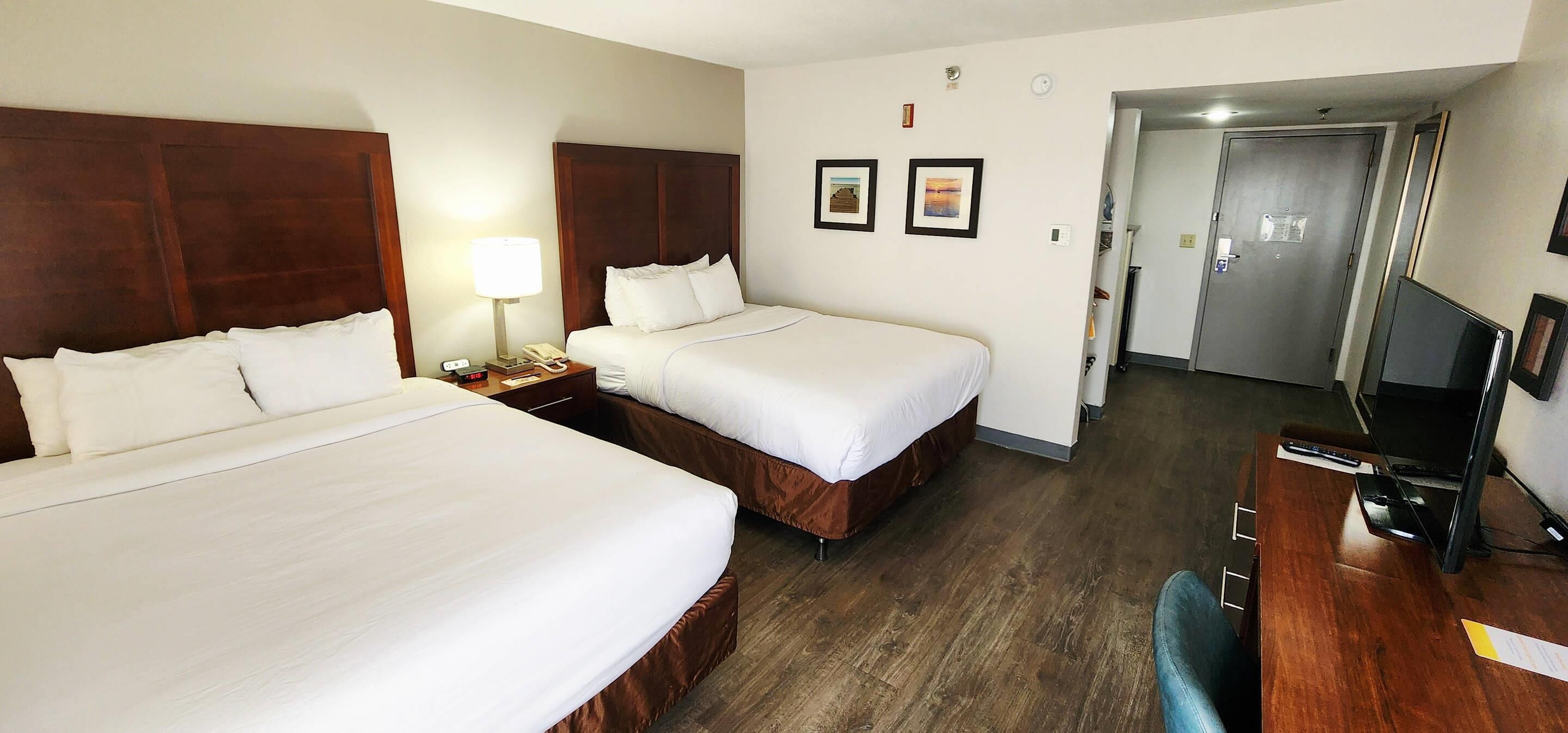 Een hotelkamer met twee bedden, een bureau met stoel, een televisie en een deur naar een andere kamer.