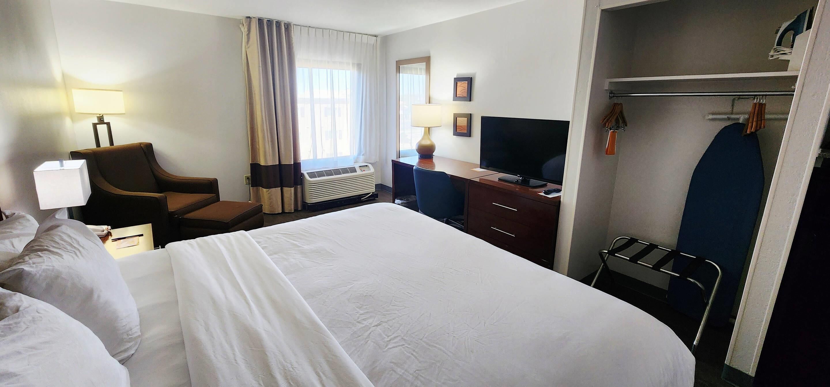 A hotel room with a bed, a desk with a computer, a chair, a TV, and a wardrobe.