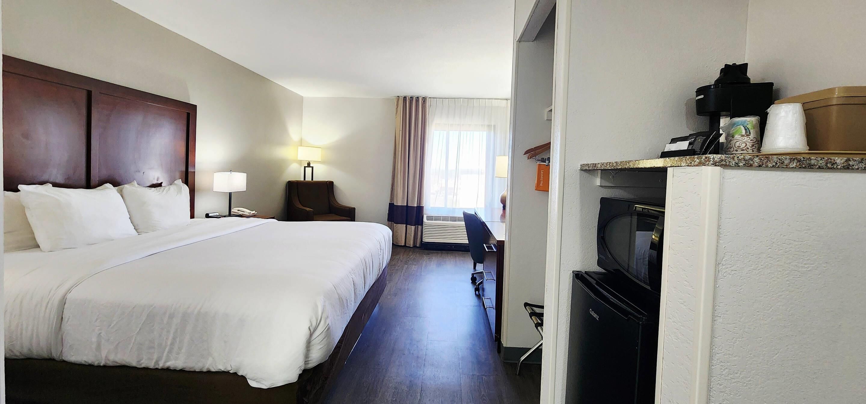 Camera d'albergo con un letto grande, una scrivania con una sedia, una televisione e un piccolo frigorifero.