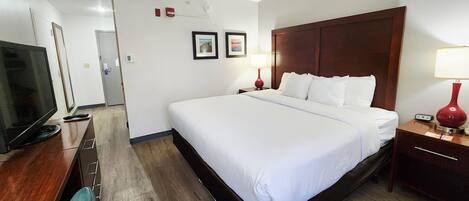 Habitación de hotel con una cama grande, televisión, escritorio con cajones, lámpara y mesita de noche con lámpara.
