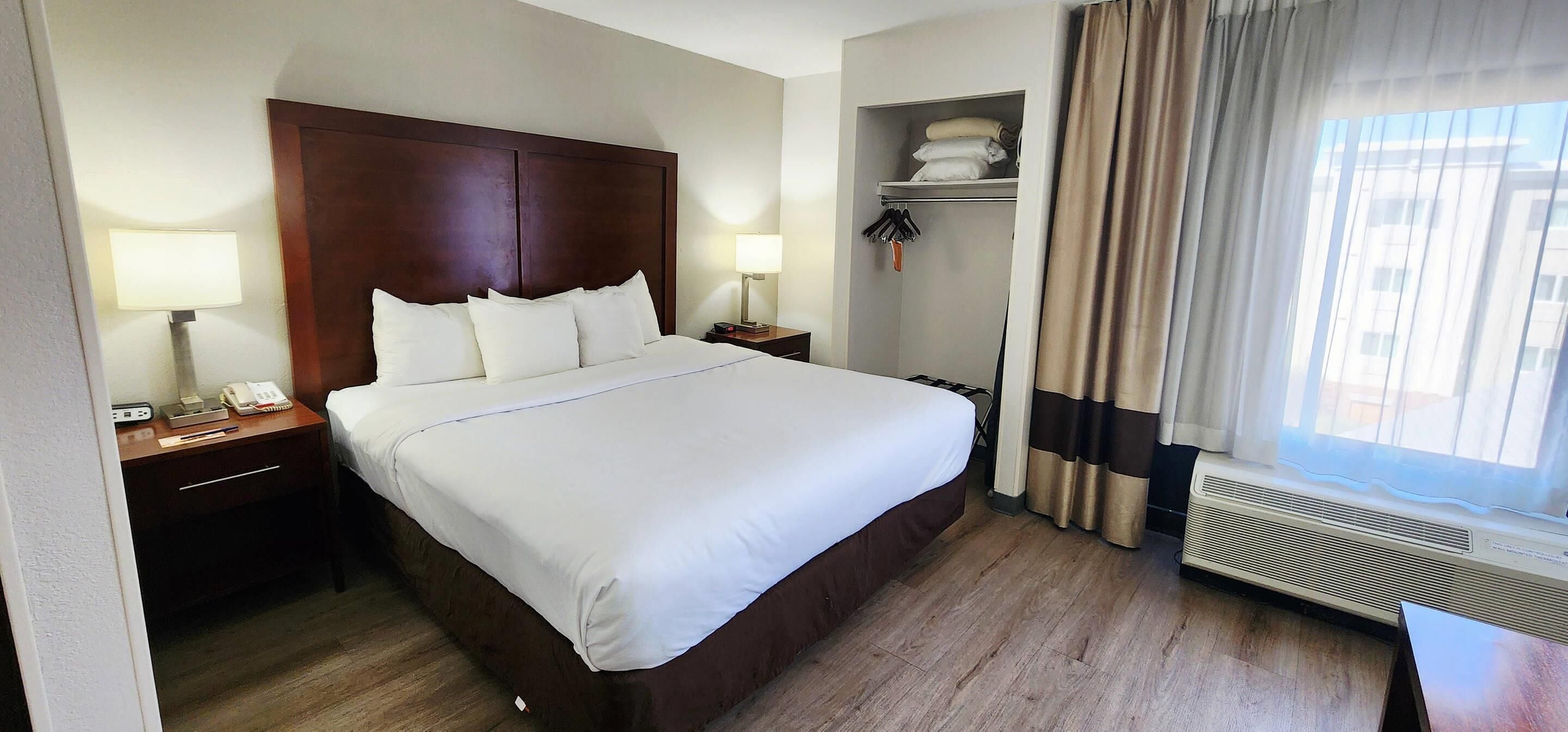 Habitación de hotel con una cama grande, lámparas de noche, mesita de noche, armario y ventana con cortinas.