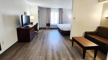 Een hotelkamer met een houten vloer, een televisie op een bureau, een bank, een bed en een raam met gordijnen.