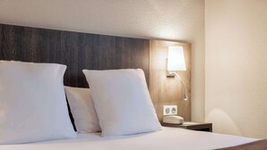 Une chambre d’hôtel avec une tête de lit en bois, une lampe de chevet et un téléphone sur une table de chevet.