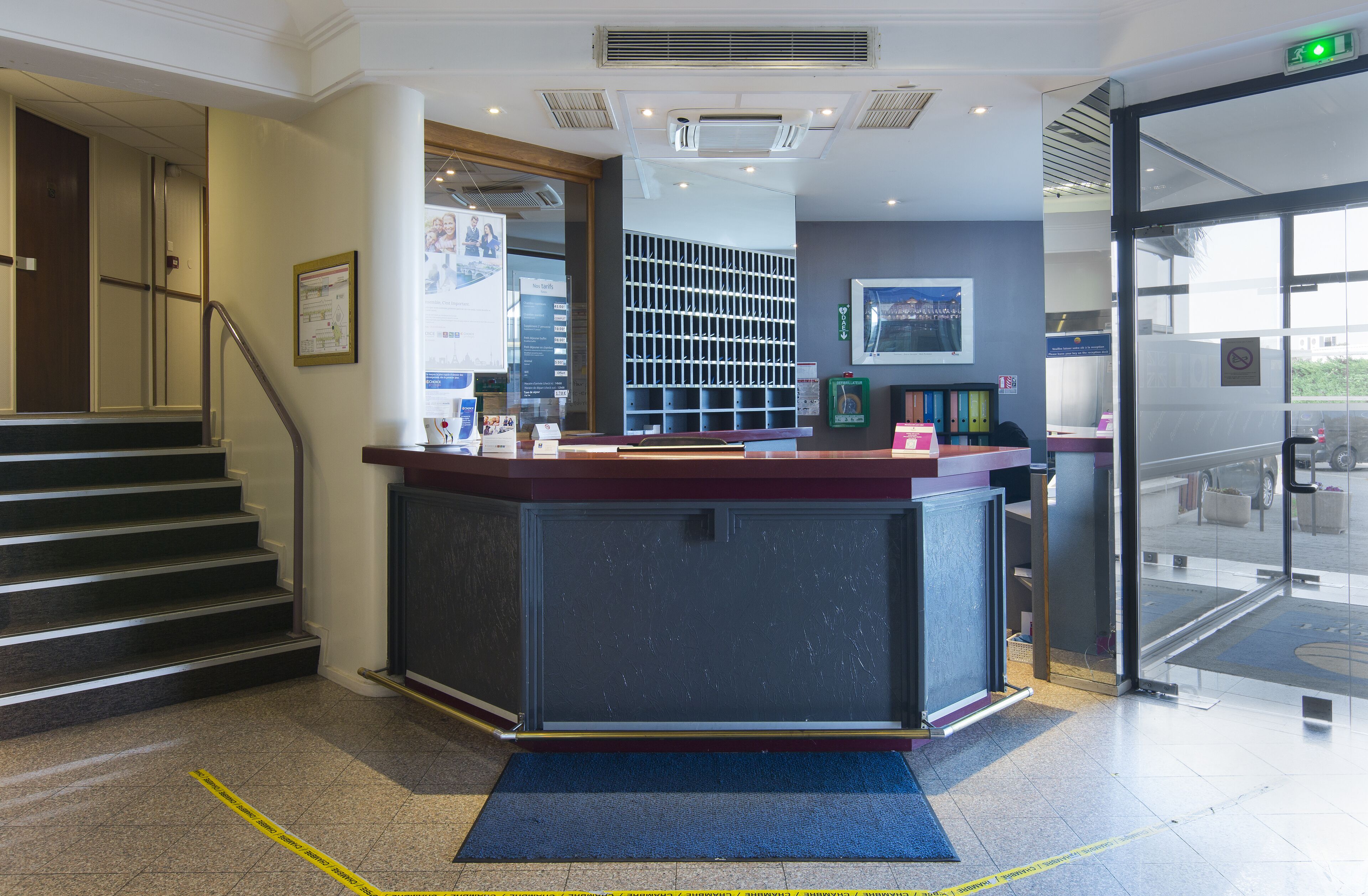 Zona de recepción con mostrador, escalera y puerta de cristal que da al exterior.