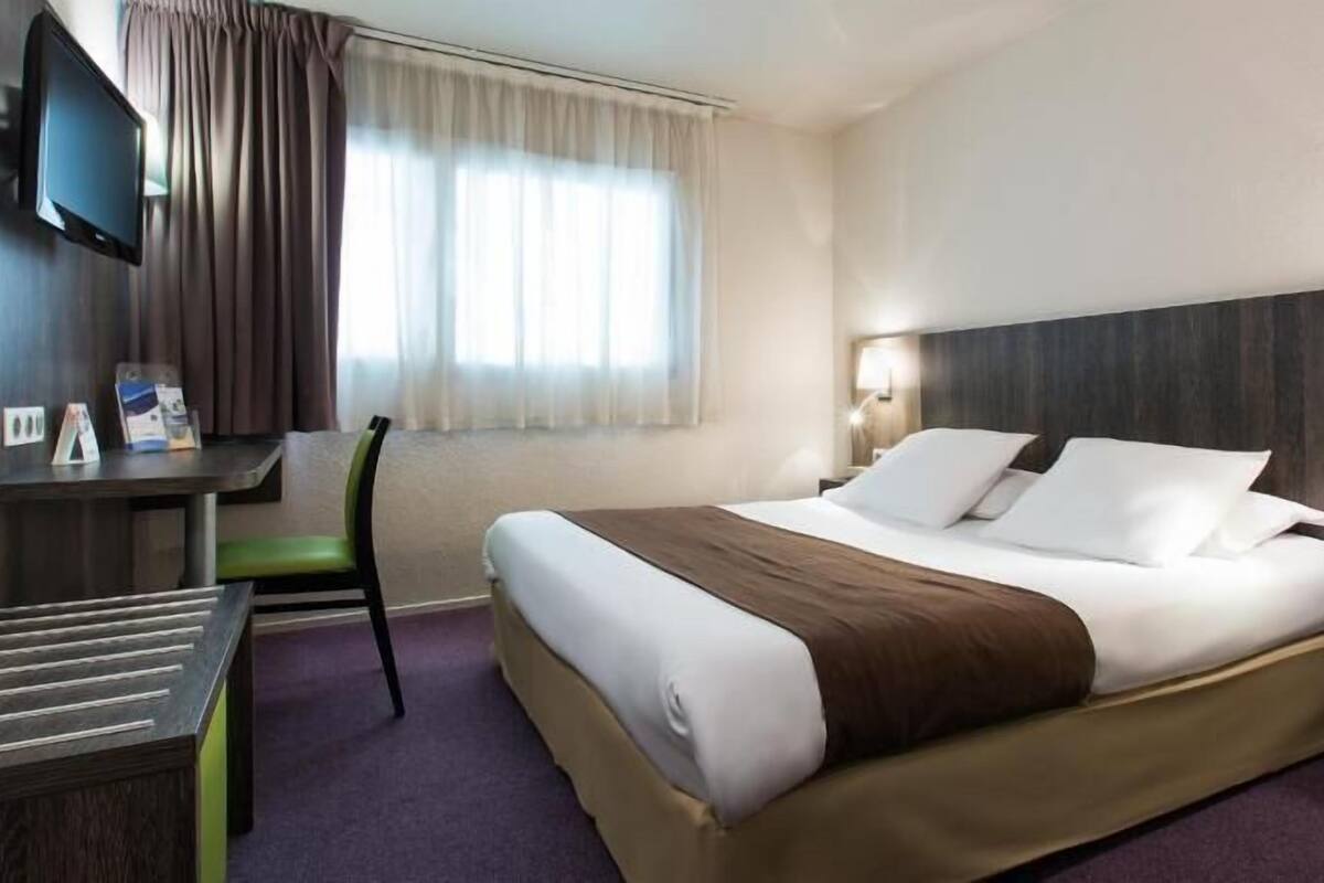 Ein Hotelzimmer mit einem Bett, einem Schreibtisch, einem Sessel, einem Fernseher und einem Fenster mit Vorhängen.