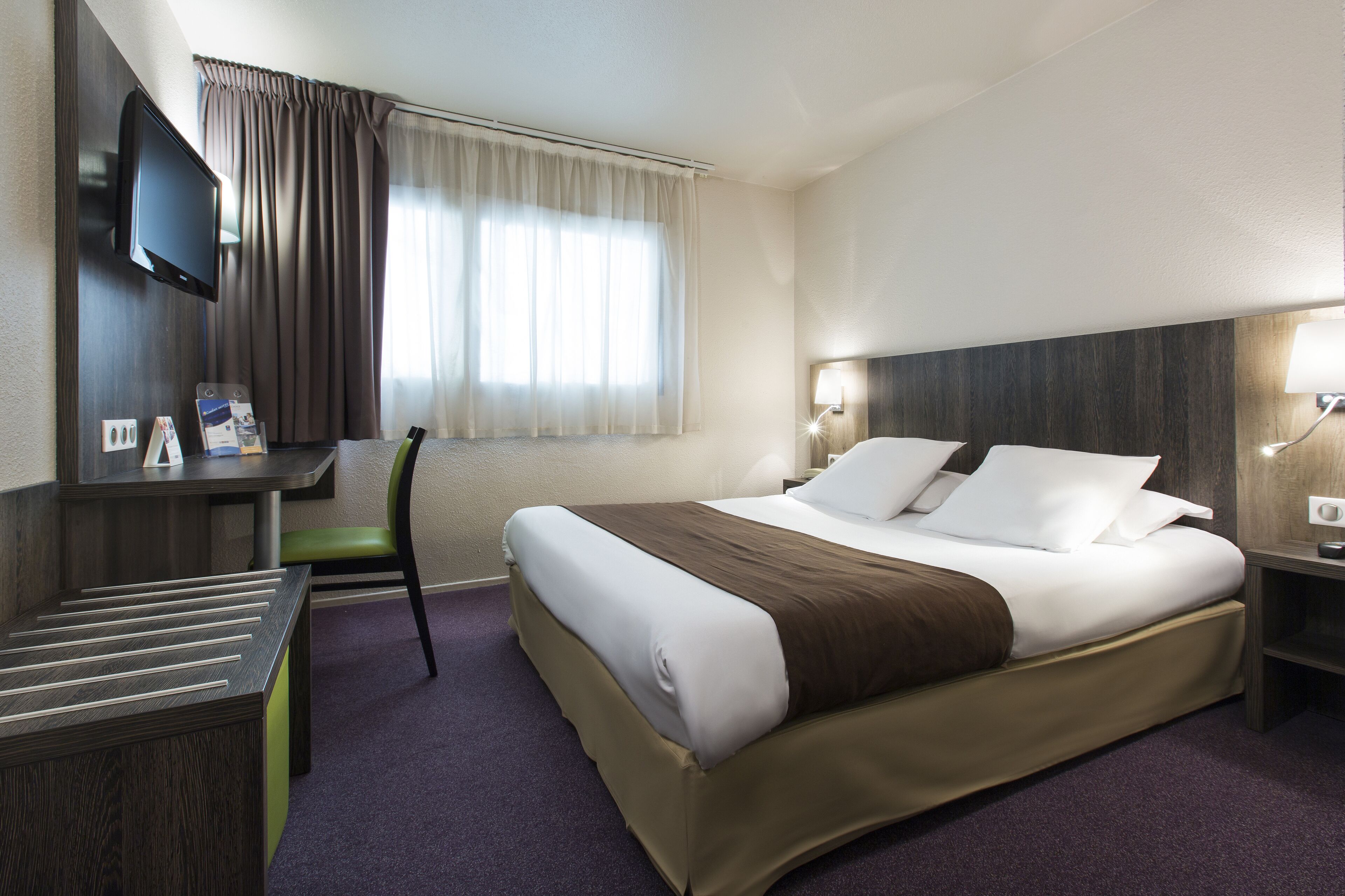 Hotelkamer met een groot bed, een bureau, een stoel, een televisie en een raam met gordijnen.