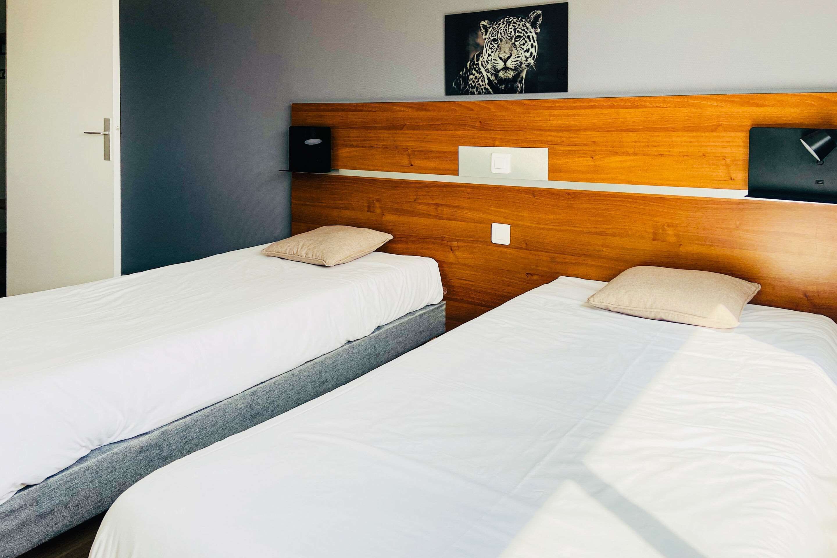 A hotel room with two beds, a wooden headboard, a leopard print artwork, and a small table with a lamp.