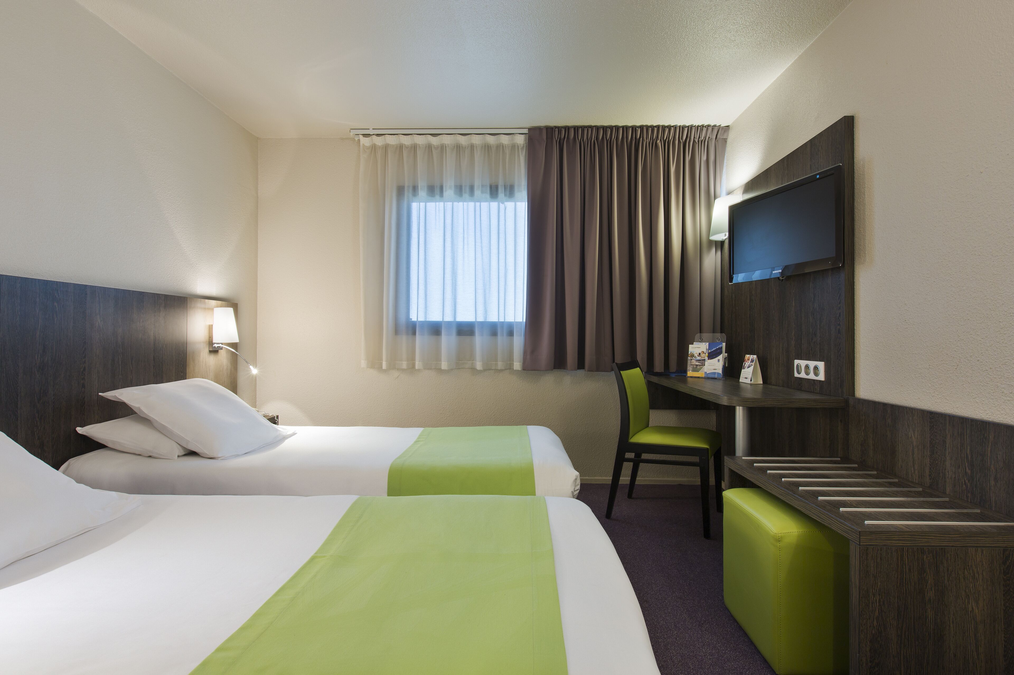 Habitación de hotel con dos camas, un escritorio, una silla, un televisor y una ventana con cortinas.