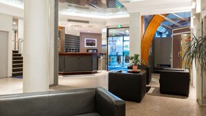 Un hall d’hôtel moderne avec un comptoir d’accueil, des espaces de détente et une vue sur la rue.