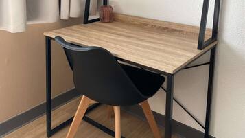 A wooden desk with a black chair, a vase, and a white wall.