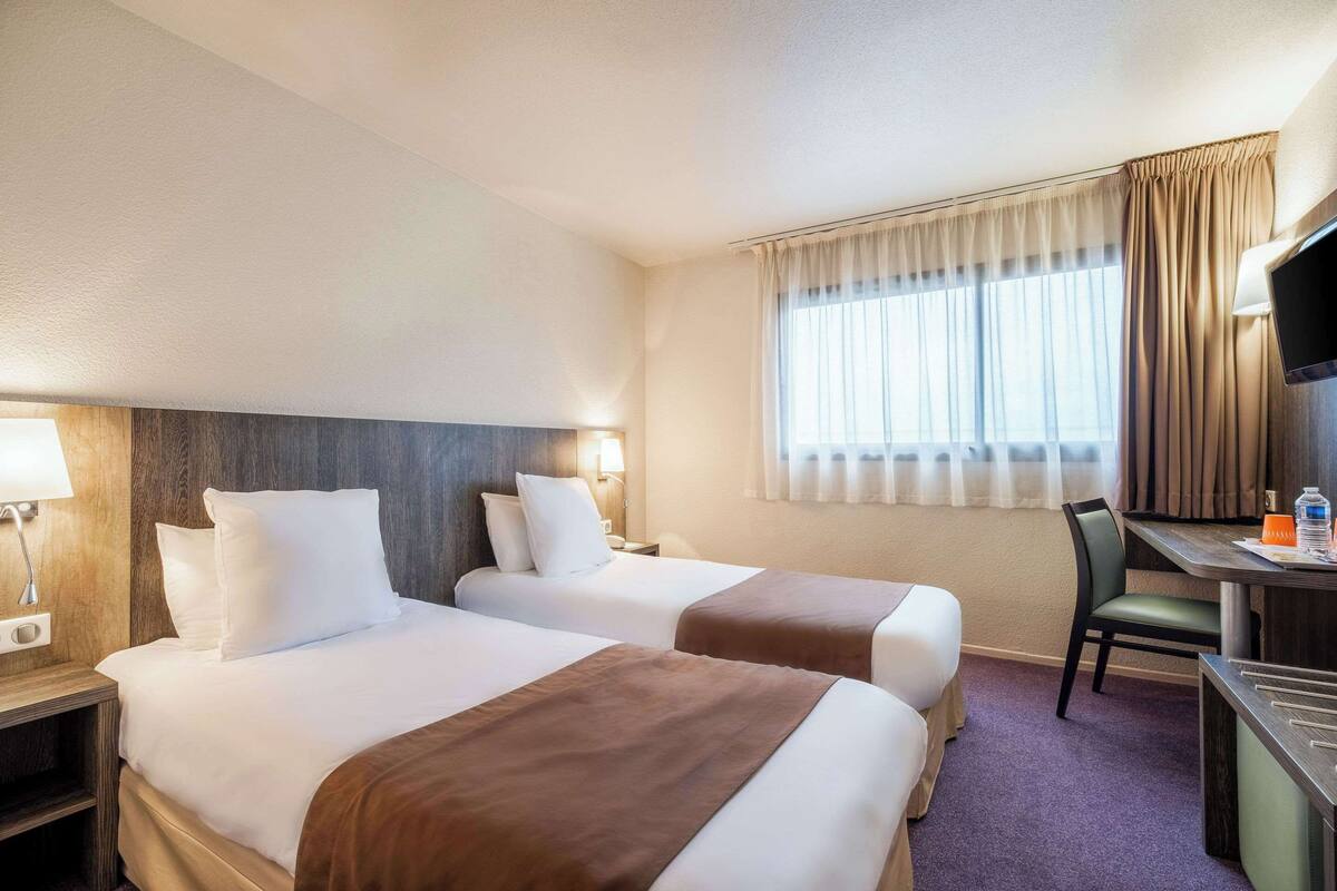 Ein Hotelzimmer mit zwei Betten, einem Schreibtisch, einem Stuhl und einem Fernseher.