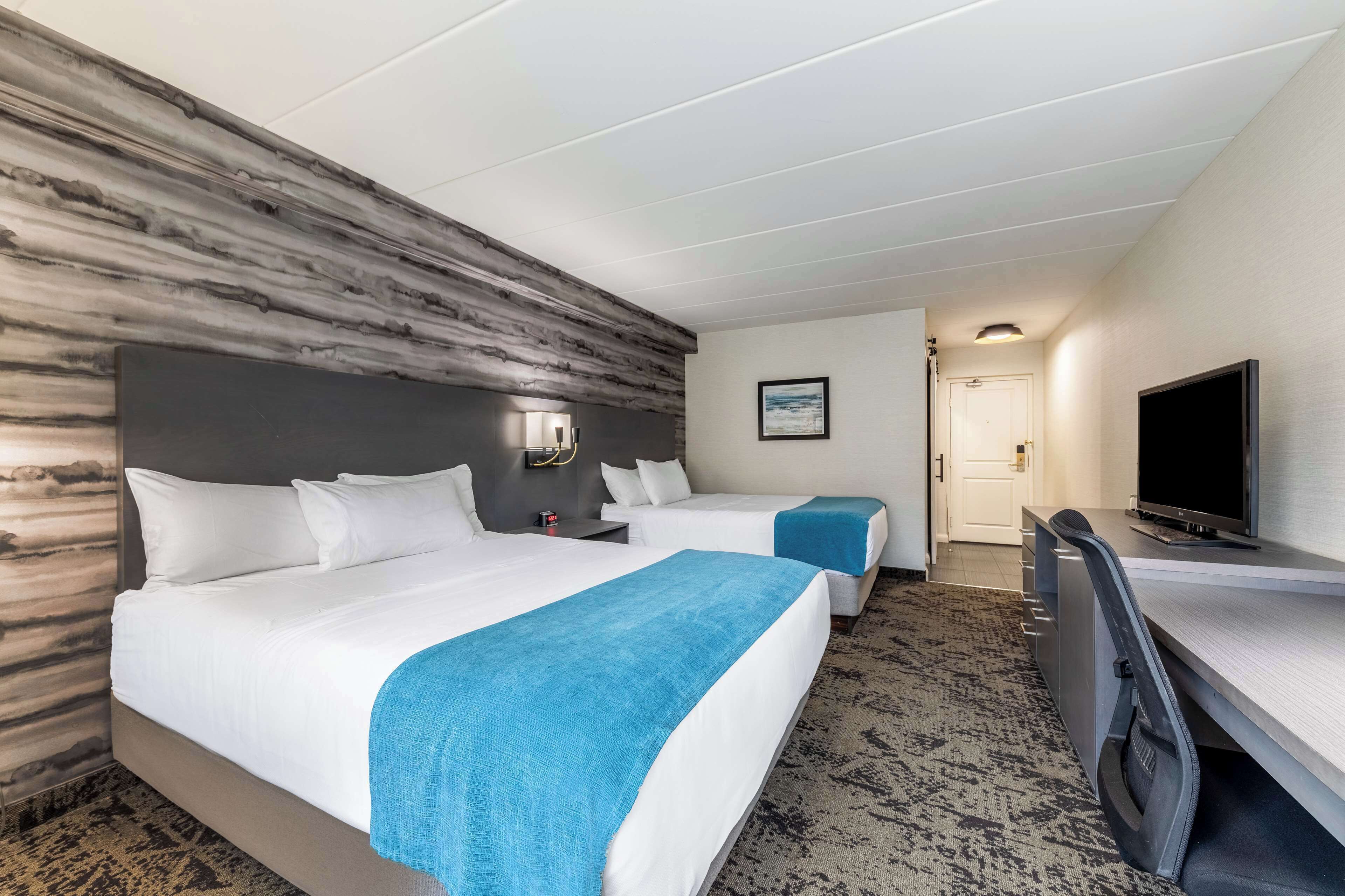 Une chambre d’hôtel avec deux lits, un bureau, une télévision et une moquette à motifs.