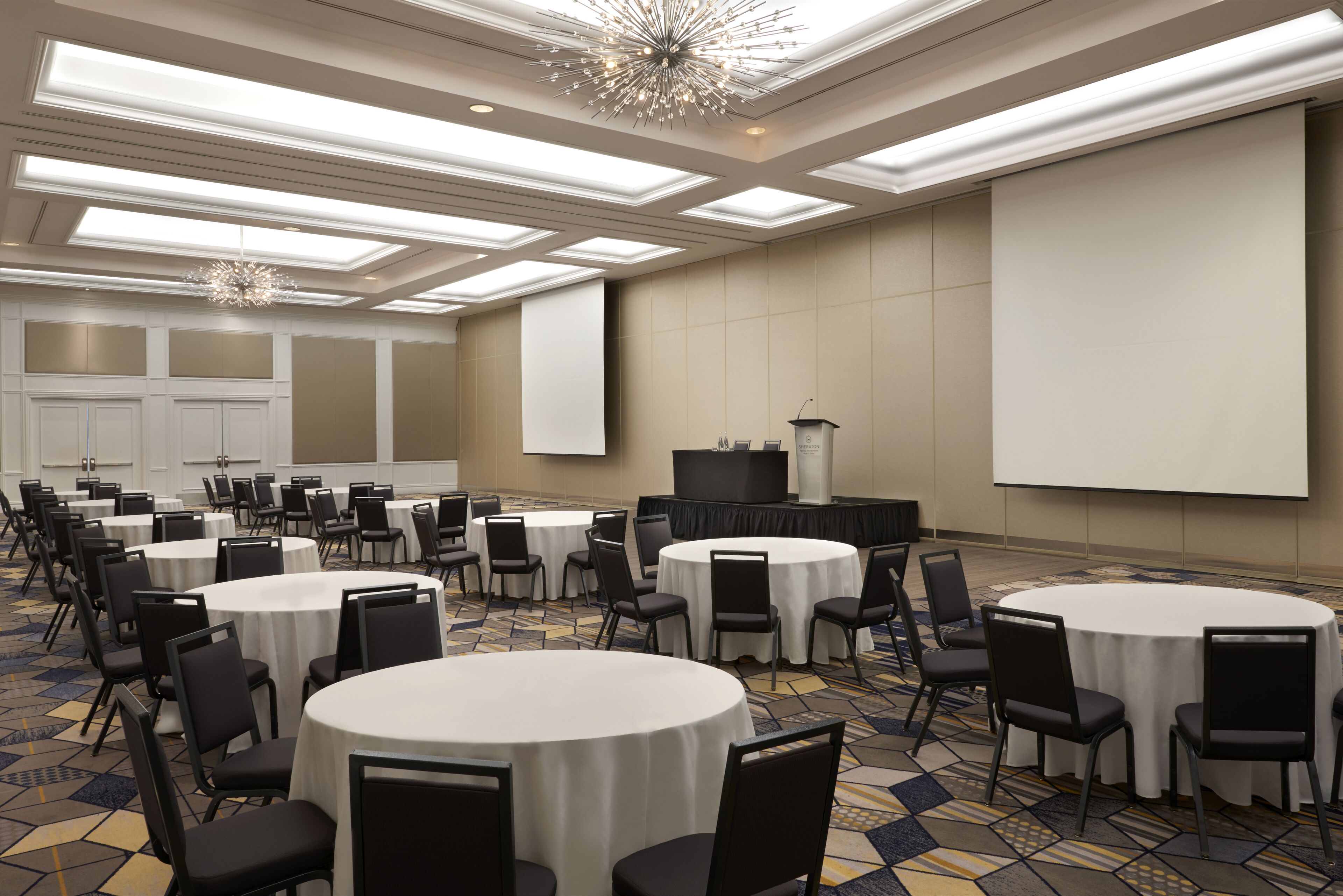 Un salón de conferencias con varias mesas redondas, sillas, un atril y una pantalla grande.