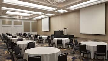 Un salón de conferencias con varias mesas redondas, sillas, un atril y una pantalla grande.
