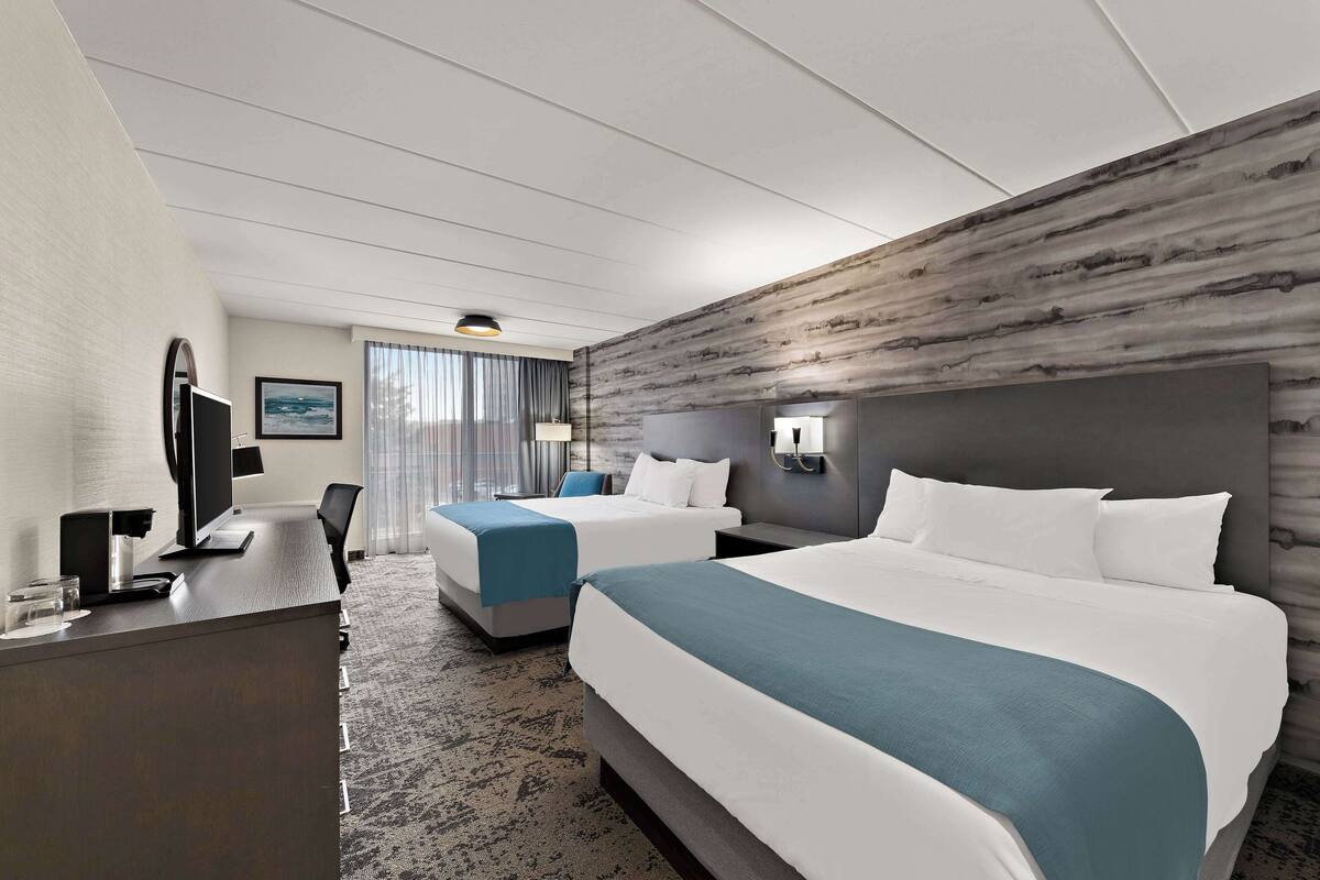 Habitació d'hotel amb dos llits, escriptori, televisió i una finestra gran amb cortines.