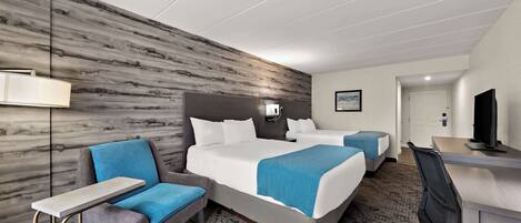 A hotel room with two beds, a desk, a chair, a lamp, and a television.