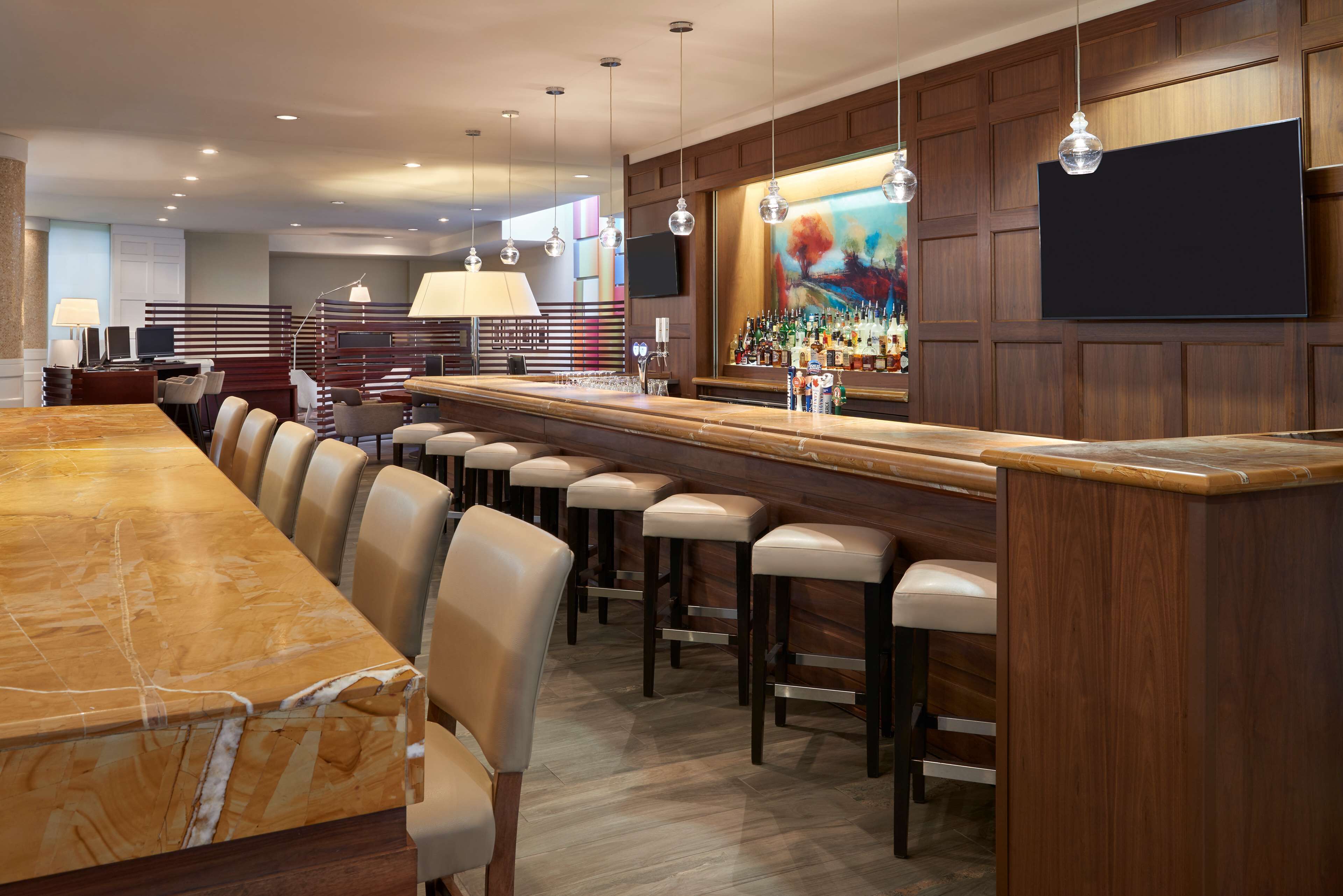 A modern bar area with a marble countertop, bar stools, and a variety of bottles.