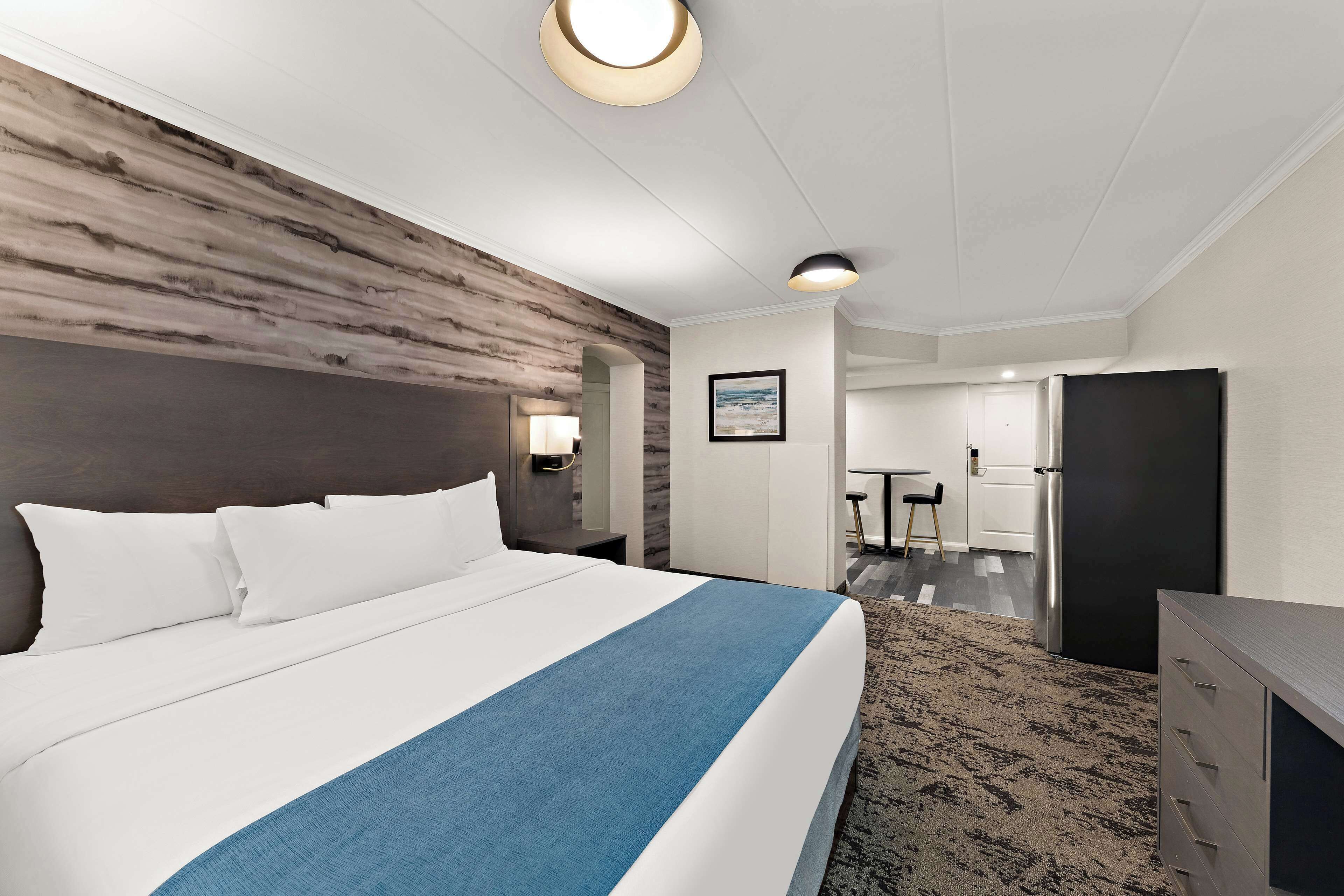 A hotel room with a large bed, a wooden accent wall, a desk, and a door leading to a bathroom.