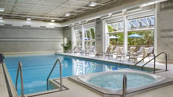 Relax by the pool with lounge chairs and umbrellas, surrounded by a hot tub and large windows.