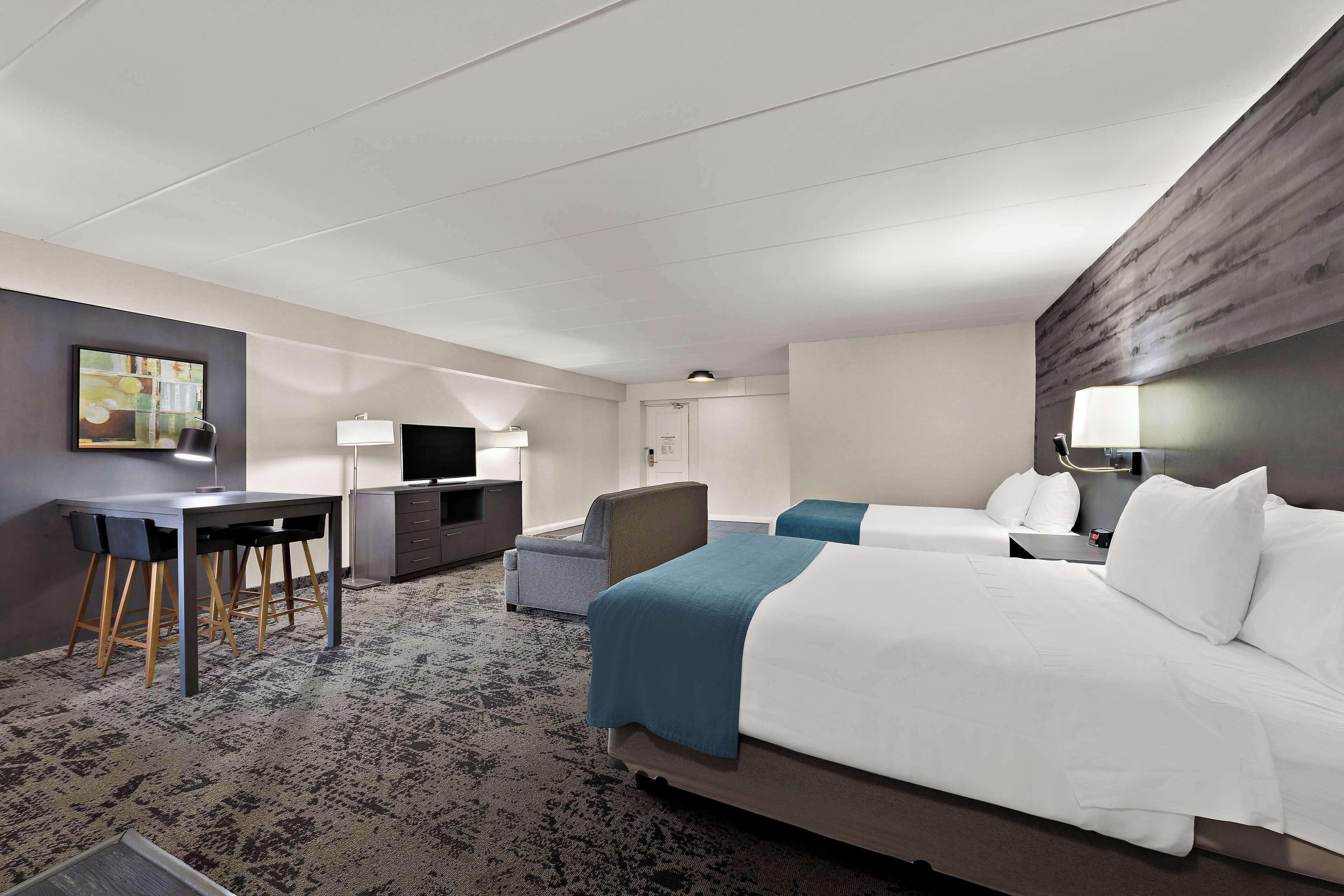 Ein Hotelzimmer mit zwei Betten, einem Schreibtisch mit Stuhl, einem Fernseher und einem Bild an der Wand.