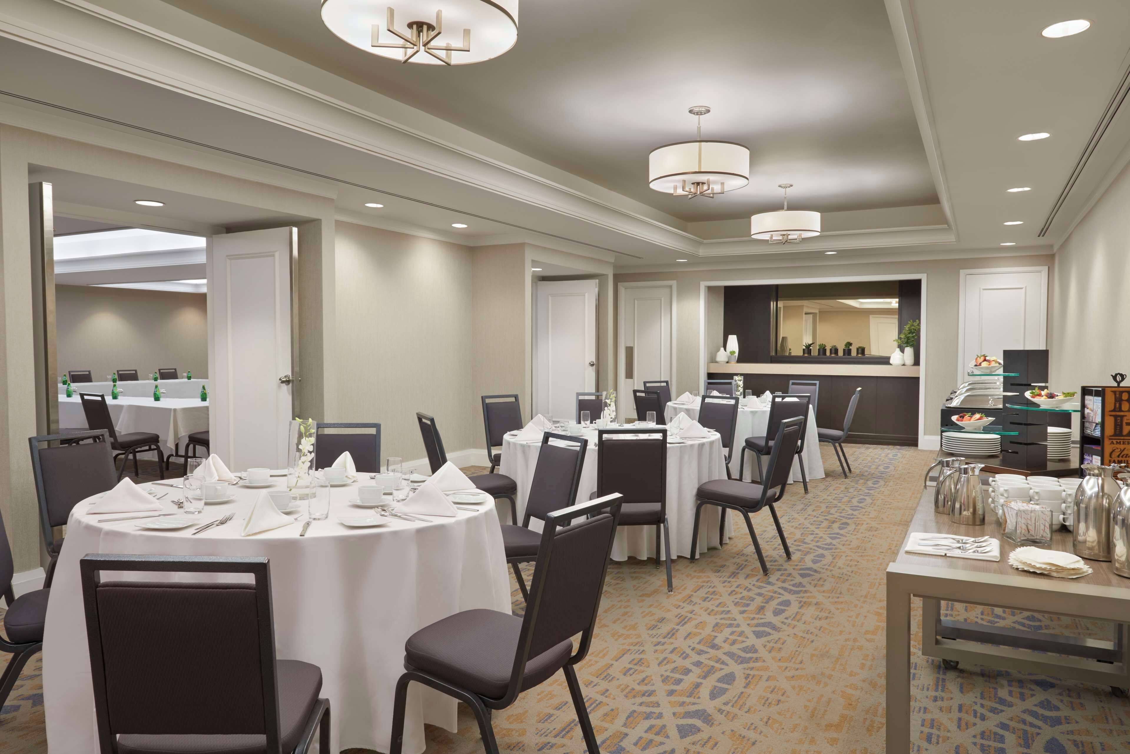 A hotel dining area with round tables, chairs, and a buffet setup.