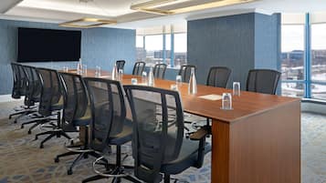 A conference room with a long table, chairs, a large screen, and a view of the city through large windows.