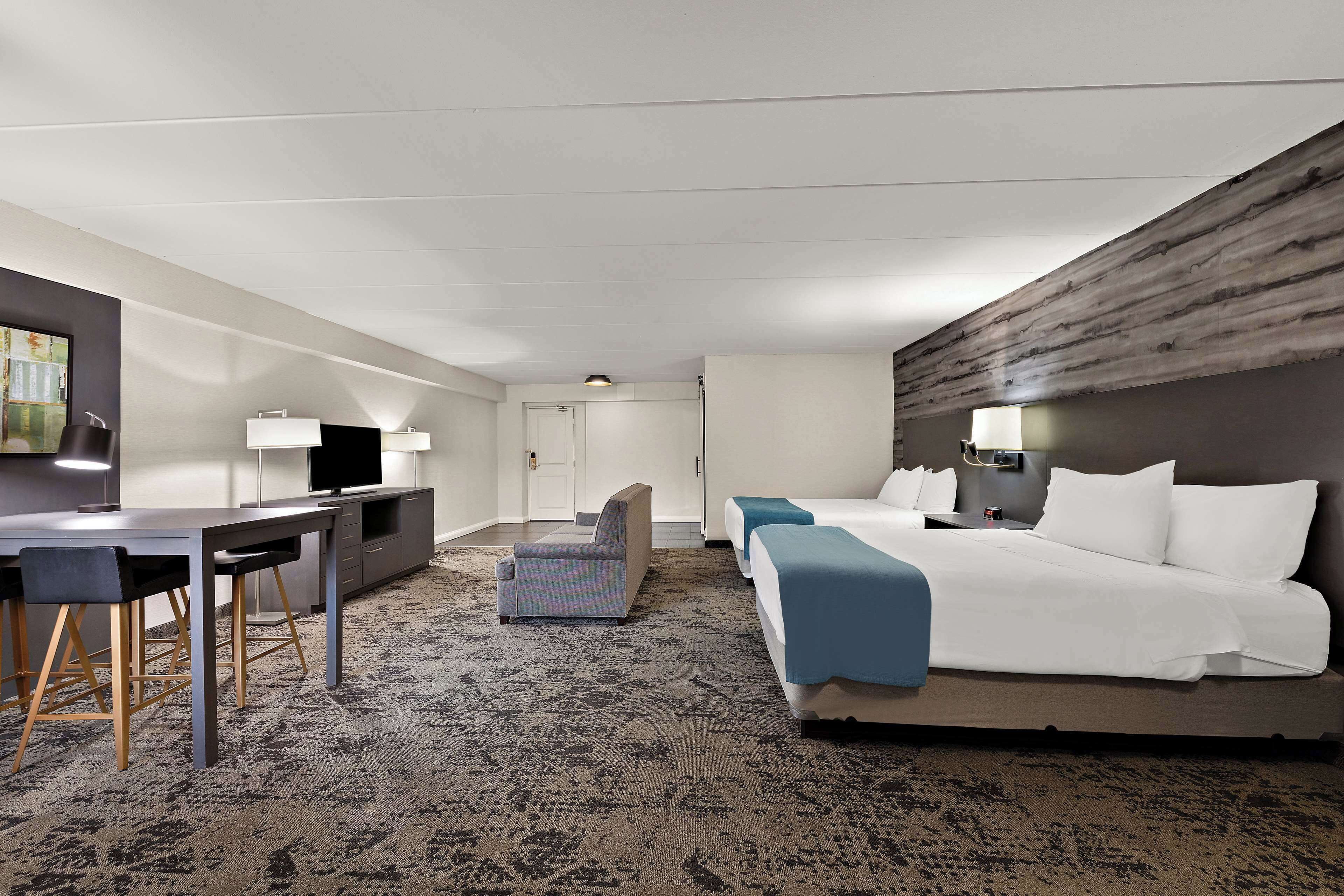 A hotel room with a large bed, a desk with two chairs, a television, and a small seating area.
