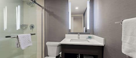 Un baño moderno con ducha de vidrio, inodoro blanco, tocador con espejo y toallero.