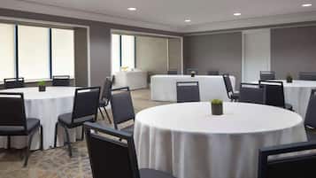 Una sala conferenze con tavoli e sedie rotonde, ampie finestre e pavimento rivestito di moquette.