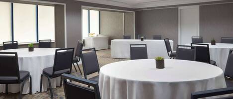 A conference room with round tables and chairs, large windows, and a carpeted floor.