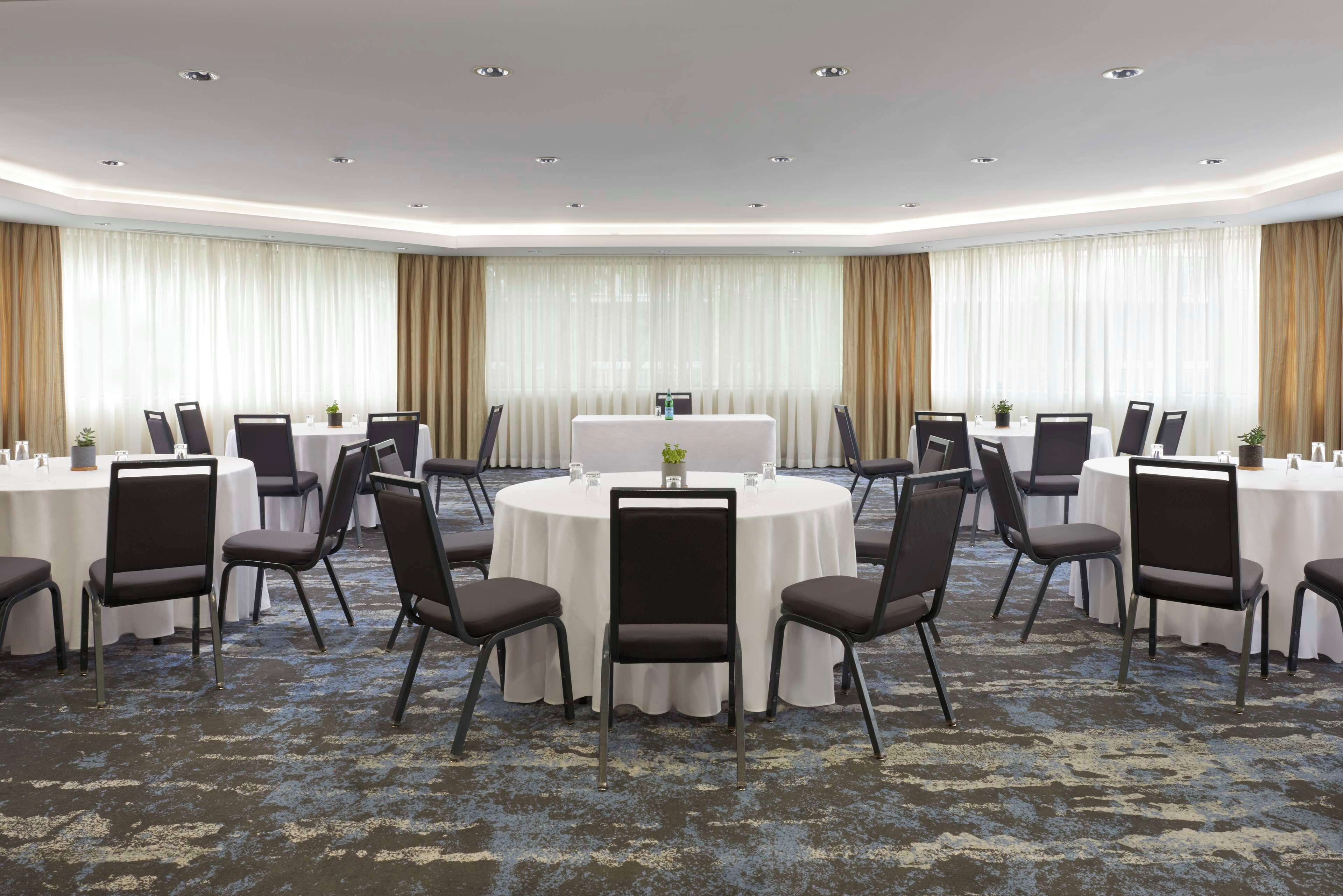 A conference room with round tables, black chairs, and a white tablecloth.