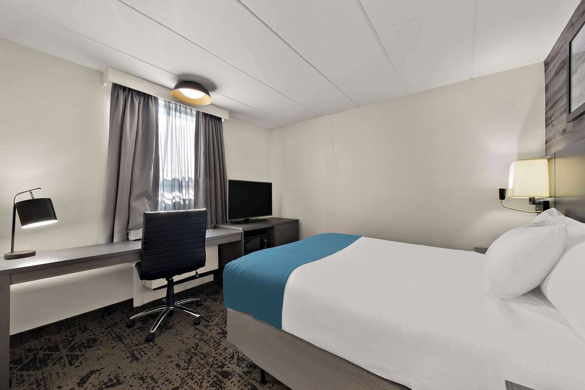 Habitació d'hotel amb llit, escriptori, cadira, televisió i làmpada.