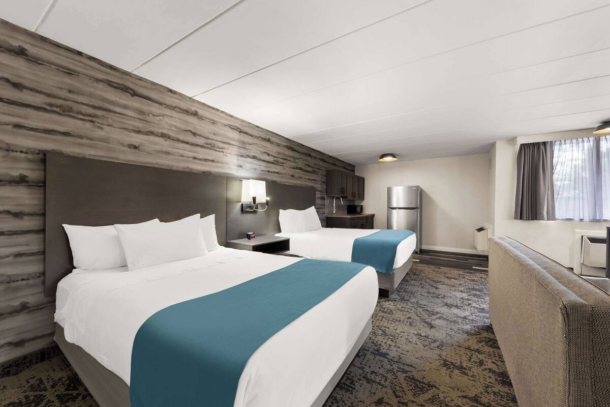 Habitació d'hotel amb dos llits, una cuineta, zona de seients i una finestra gran.