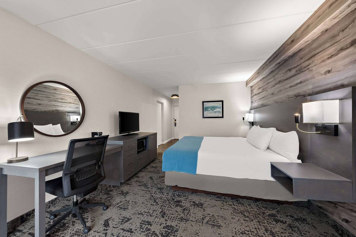 Habitació d'hotel amb llit, escriptori, cadira, televisió i un mirall gran.