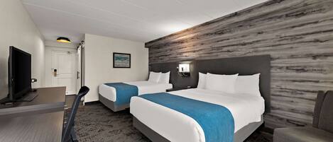 Habitación de hotel con dos camas, un escritorio, televisor y una lámpara fijada a la pared.