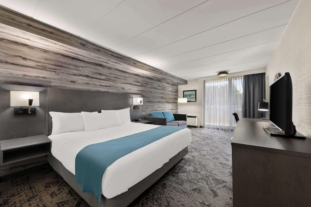 Una habitación de hotel moderna con una cama grande, un escritorio, un televisor de pantalla plana y una zona de estar con un sofá y sillones.