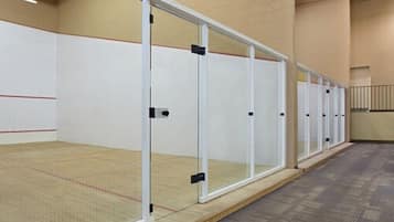 A squash court with glass doors, a wooden floor, and a carpeted hallway.
