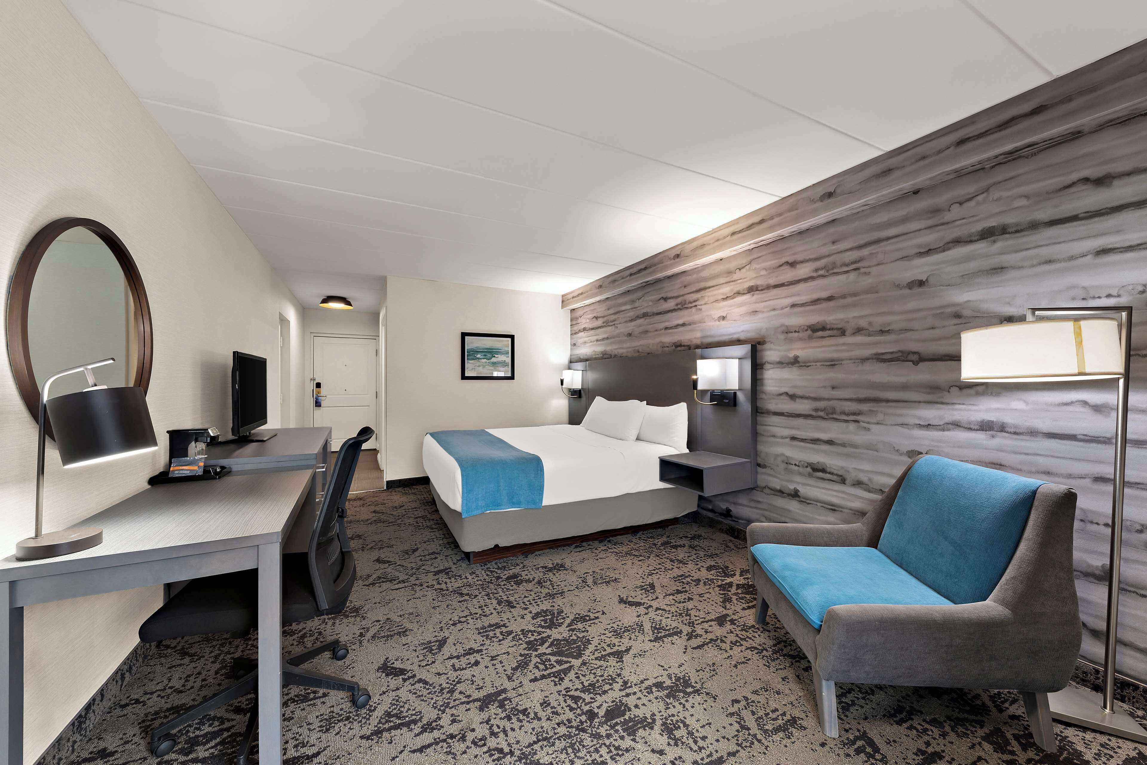 Hotellihuone, jossa on sänky, työpöytä, tuoli ja suuri peili.
