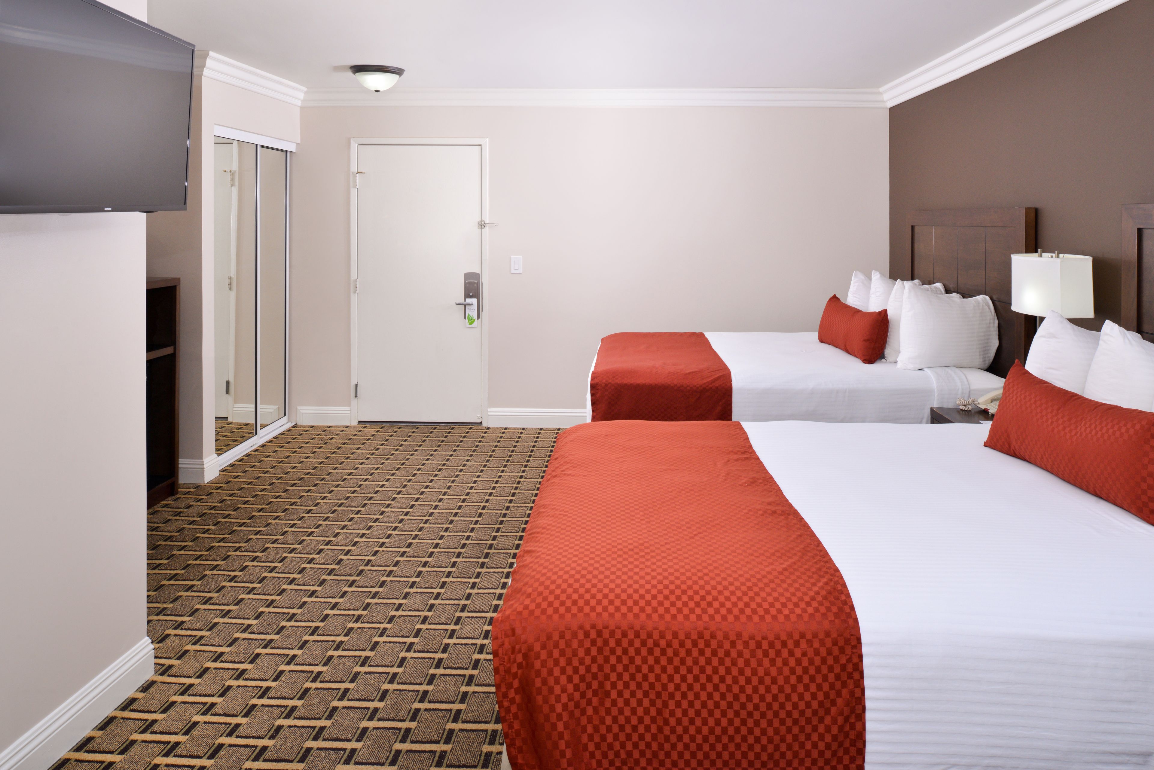 A hotel room with two beds, a television, and a door.
