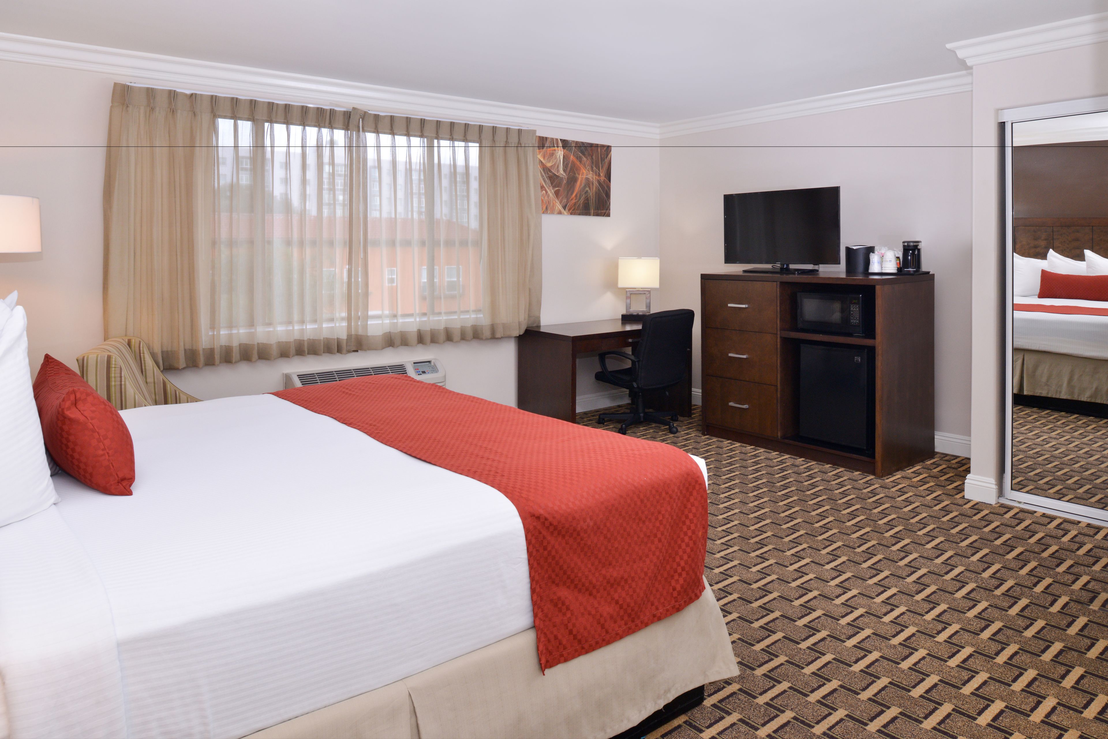 Ein Hotelzimmer mit einem großen Bett, einem Schreibtisch, einem Fernseher und einem Kleiderschrank.