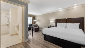 A hotel room with a large bed, a desk with a chair, a small table with a lamp, and a bathroom with a shower and toilet. - Best Western Plus LA Mid Town Hotel (Los Angeles)