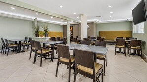 A spacious dining area with multiple tables and chairs, recessed ceiling lights, and a large flat-screen TV mounted on the wall. - Best Western Plus LA Mid Town Hotel (Los Angeles)