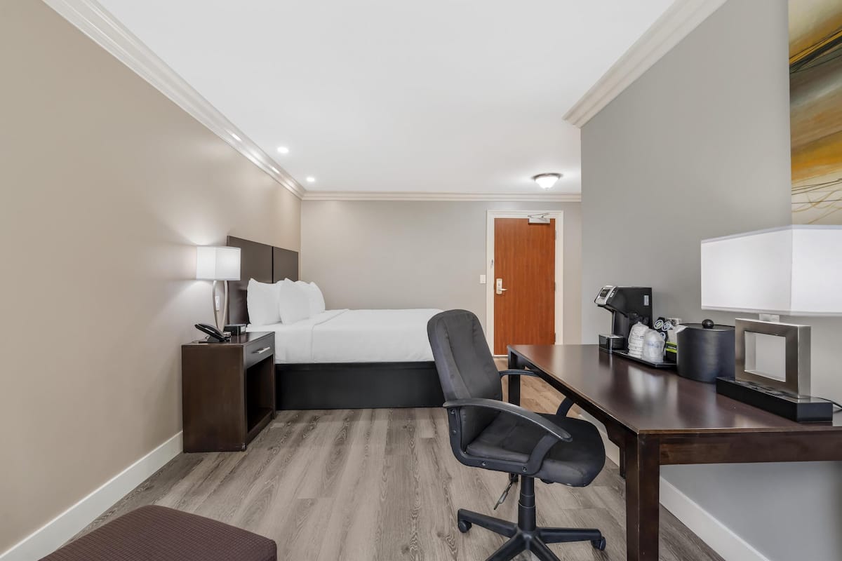 A hotel room with a bed, desk, chair, and a coffee machine.